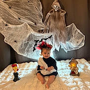 Elya participe au concours pour gagner de l'argent avec cette photo : baby, bat, black_clothing, child, cobwebs, costume, cute, decoration, ghost, glowing_lights, halloween, headband, holiday, indoor, portrait, props, skull, smile, spiders, white_blanket