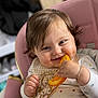 baby, child, high_chair, orange, food, bib, smile, happy, messy, bracelet, clothing, face, hand, hair, indoor, person, cute, juice, eating, infant
