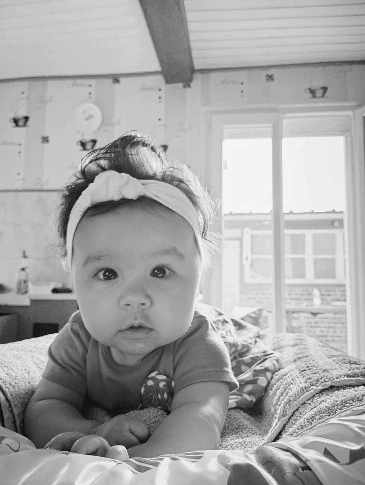 Marion a rejoint le concours — aidez-le/la à gagner de superbes lots ! baby, headband, bed, blanket, indoor, infant, face, curious, wide_eyes, portrait, monochrome, soft_lighting, clothing, hand, wallpaper, window, room, cozy, child, person