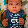 baby, infant, child, blue_onesie, text_on_clothing, animal_print, blanket, cute, portrait, indoors, pacifier, hands, face, wide_eyes, looking_at_camera, soft_lighting, adorable, young_child, comfortable, baby_bedding