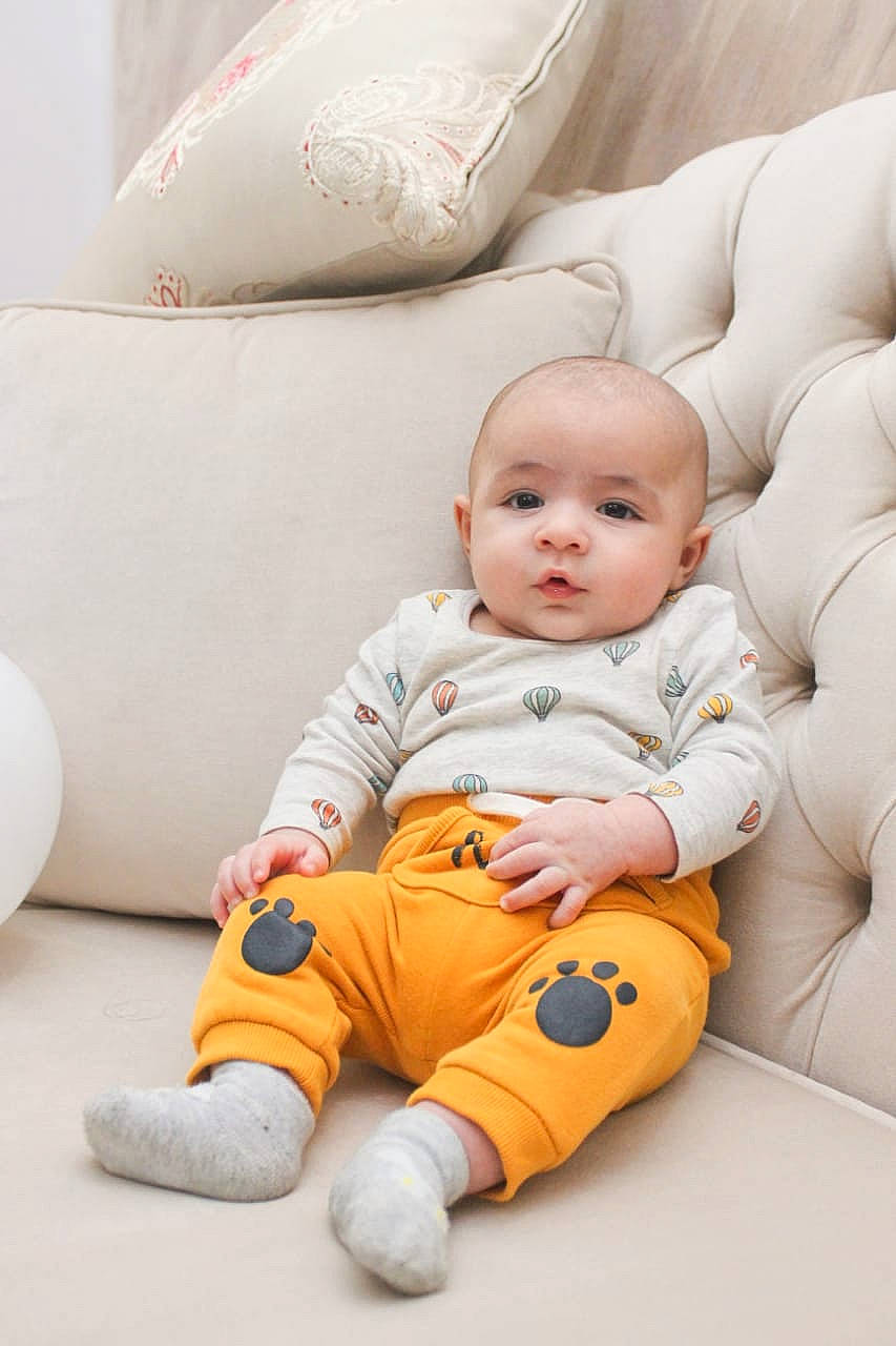 Iyed participe au concours pour gagner de l'argent avec cette photo : baby, baby_toddler_clothing, cheek, comfort, eye, face, floor, flooring, happy, head, knee, leg, orange, person, product, skin, sleeve, textile, toddler, white