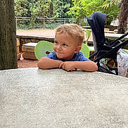 Arthur participe au concours pour gagner de l'argent avec cette photo : child, toddler, smile, table, outdoor, greenery, tree, stroller, chair, playful, face, person, nature, park, daylight, expression, casual, relaxing, cute, curly_hair