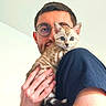 Baelor participe au concours pour gagner de l'argent avec cette photo : blue_eyes, casual_clothing, cat, close_up, cute, face, fur, glasses, hand, holding, indoor, kitten, light_skin, looking_at_camera, man, pet, portrait, short_hair, striped_fur, young_adult