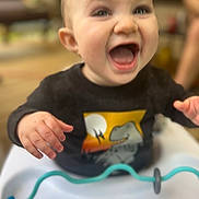 Roman joined the competition — help win amazing prizes! baby, child, smiling, dinosaur, black_shirt, high_chair, toy, happy, indoor, hands, face, mouth_open, cute, infant, playful, clothing, person, expression, closeup, seated