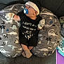 baby, infant, pacifier, beanie, mittens, socks, nursing_pillow, dinosaur_pattern, patterned_pillow, couch, sofa, onesie, black_onesie, carpet, living_room, blanket, tissue, adult_socks, home_interior, candid_photo