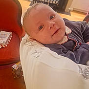 Raphaël participe au concours pour gagner de l'argent avec cette photo : baby, child, indoor, person, face, smile, clothing, arm, chair, furniture, home, holding, curly_hair, red_trim, white_collar, table, box, floor, window, curtain