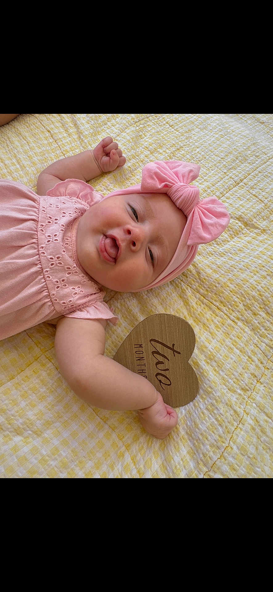 Alayah is registered to the contest to win money with this photo: baby, infant, pink_dress, headband, bow, tongue_out, yellow_blanket, wooden_sign, two_months, cute, smile, face, arm, hand, lying_down, indoors, portrait, child, happy, soft_texture