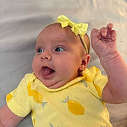 Alayah is registered to the contest to win money with this photo: baby, infant, yellow_clothing, headband, bow, tongue_out, face, cute, expression, lying_down, closeup, skin, hand, arm, person, child, soft_surface, pattern, playful, happy