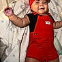 Eliana is registered to the contest to win money with this photo: baby, infant, smiling, red_overalls, headband, blanket, lying_down, cute, happy, child, indoors, cozy, soft_blanket, arm_outstretched, portrait, small_child, fashion, accessory, person, baby_bottle