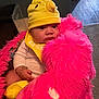 Eliana is registered to the contest to win money with this photo: baby, child, hat, yellow, bib, stuffed_animal, pink, plush, indoors, carpet, bracelet, cute, person, soft_toy, infant, clothing, toy, face, portrait, cozy