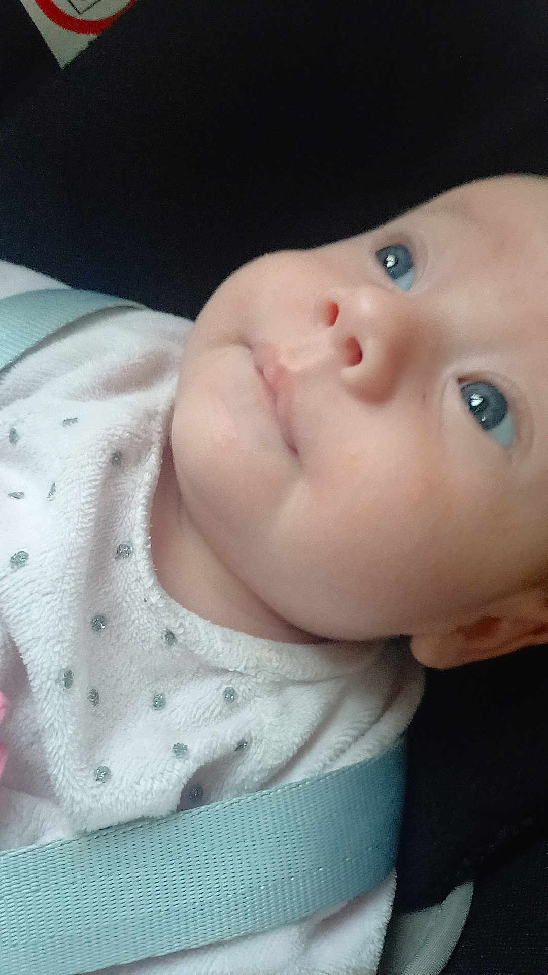 Lou participe au concours pour gagner de l'argent avec cette photo : baby, child, face, blue_eyes, white_clothing, strap, close_up, infant, portrait, skin, cute, young, looking_up, head, person, soft_texture, dots, fabric, expression, indoors