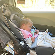 Ahvi is registered to the contest to win money with this photo: baby, infant, sleeping, car_seat, vehicle, passenger, pacifier, blanket, pink_clothing, rear_facing, travel, transportation, sunlight, window, road_trip, safety_straps, portrait, indoors, child, resting