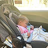 baby, infant, sleeping, car_seat, vehicle, passenger, pacifier, blanket, pink_clothing, rear_facing, travel, transportation, sunlight, window, road_trip, safety_straps, portrait, indoors, child, resting