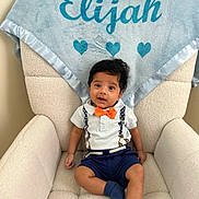 Elijah is registered to the contest to win money with this photo: baby, child, armchair, blanket, blue, bow_tie, clothing, cute, face, furniture, indoor, infant, person, portrait, sitting, smile, soft_texture, white_shirt, young_child, young_boy