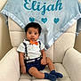 Elijah is registered to the contest to win money with this photo: baby, child, boy, indoor, chair, blanket, blue, orange_bow_tie, white_shirt, navy_shorts, socks, face, person, cute, plush, comfortable, portrait, expression, decor, home