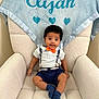 Elijah is registered to the contest to win money with this photo: baby, child, infant, chair, blanket, blue, orange_bow_tie, smiling, cute, plush, comfortable, indoors, portrait, clothing, socks, seated, person, happy, decor, young