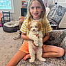 Dolce joined the competition — help win amazing prizes! child, dog, puppy, couch, living_room, carpet, window, person, furniture, smiling, blonde_hair, striped_shirt, orange_shorts, pet, indoor, cute, seated, holding, happy, house