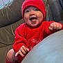baby, bright, child, couch, cozy, cute, face, hands, happy, holiday_style, indoor, infant, knitwear, leather_furniture, portrait, red_hat, red_sweater, seated, smiling, warm_clothing