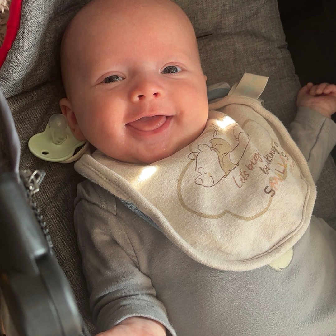 Mikey-Rhys is registered to the contest to win money with this photo: baby, bib, child, closeup, comfort, cushion, cute, face, gray_clothing, happy, indoors, infant, lying_down, newborn, pacifier, plush_toy, portrait, smiling, soft_light, warm