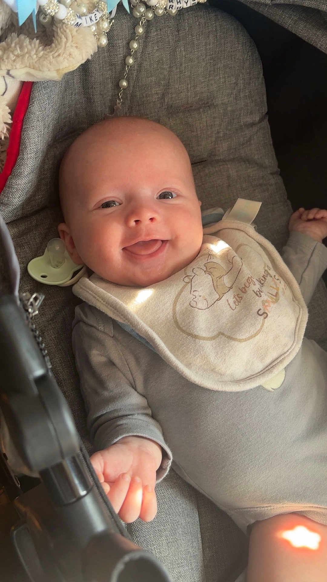 Mikey-Rhys is registered to the contest to win money with this photo: baby, smiling, infant, bib, gray_clothing, pacifier, cushion, face, happy, cute, lying_down, indoors, soft_light, plush_toy, closeup, child, portrait, newborn, warm, comfort