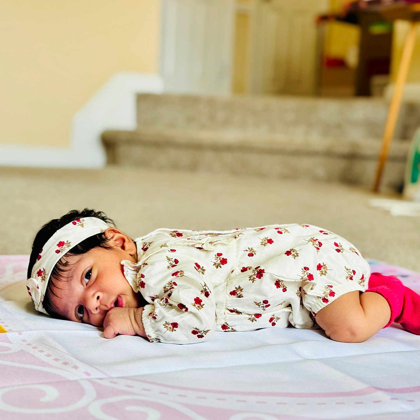 Anshika is registered to the contest to win money with this photo: baby, blanket, carpet, child, cozy, cute, face, floral_outfit, headband, home, indoors, infant, looking, lying_down, person, pink_socks, portrait, resting, soft_lighting, young_child