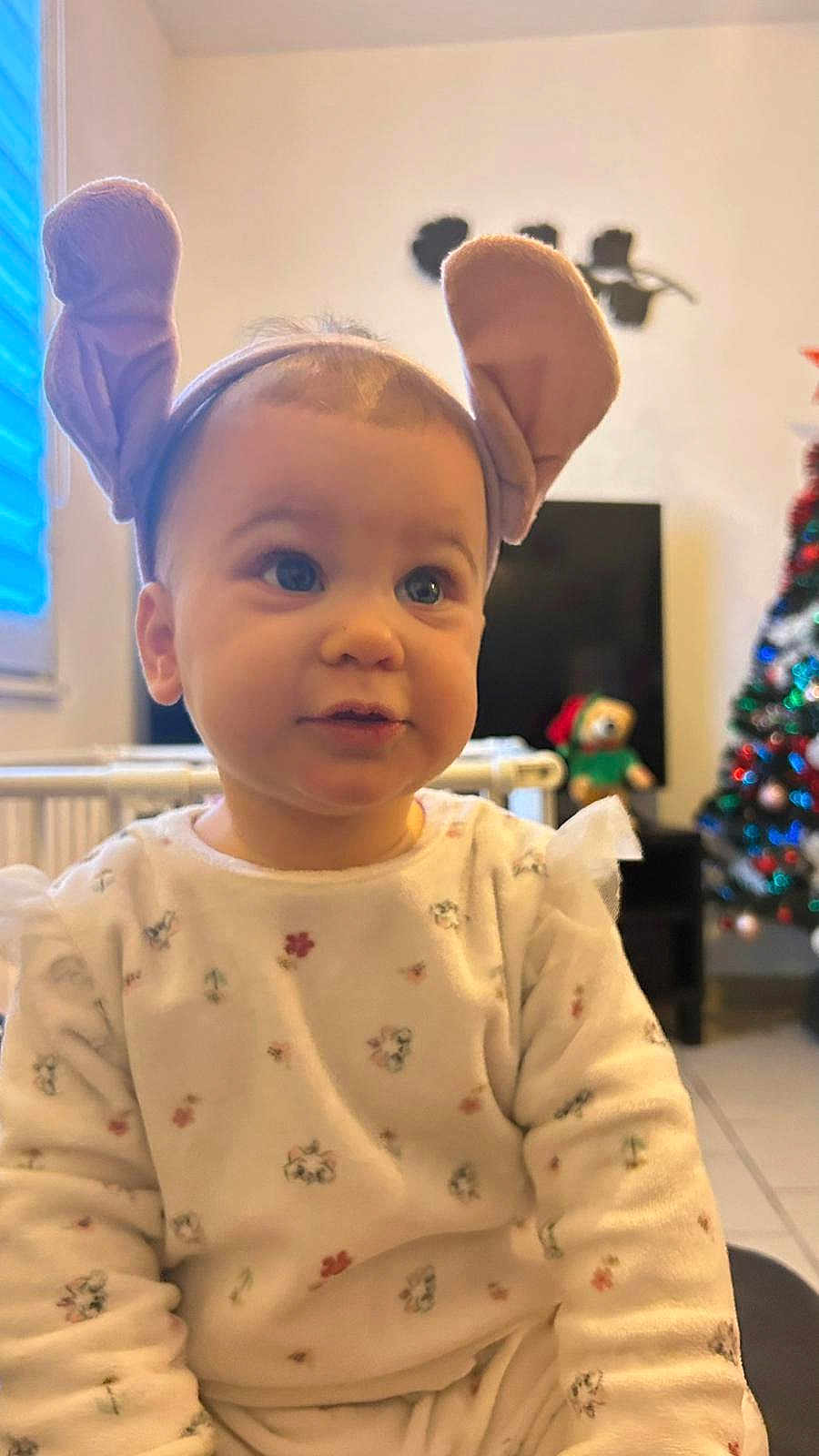 Ella participe au concours pour gagner de l'argent avec cette photo : baby, bunny_ears, child, christmas_tree, cozy, cute, decor, expression, floor_tiles, floral_pattern, furniture, headband, holiday, indoor, person, portrait, sitting, soft_lighting, teddy_bear, window