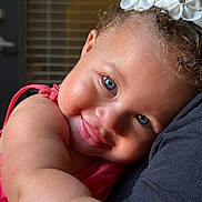 Elise joined the competition — help win amazing prizes! toddler, child, blue_eyes, curly_hair, flower_hair_clip, pink_clothing, close_up, face, smile, skin, arm, cuddling, affection, indoor, portrait, happy, cute, baby, person, head