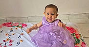 Louna a rejoint le concours — aidez-le/la à gagner de superbes lots ! baby, child, smiling, purple_dress, flower, blanket, indoor, tiled_floor, cute, portrait, happy, sitting, decoration, floral_pattern, infant, person, celebration, bright_colors, adorable, toddler