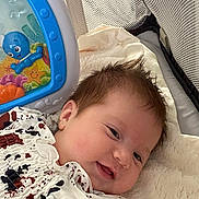 Aurora is registered to the contest to win money with this photo: baby, blanket, child, closeup, cute, face, happy, head, indoor, infant, lying_down, mesh, octopus, patterned_clothing, playpen, smiling, soft_texture, starfish, toy, young_child