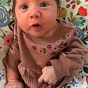 Aurora joined the competition — help win amazing prizes! baby, infant, child, face, eyes, expression, clothing, embroidered, sleeves, hand, fingers, cushion, pattern, floral, colorful, seated, portrait, indoors, cute, young