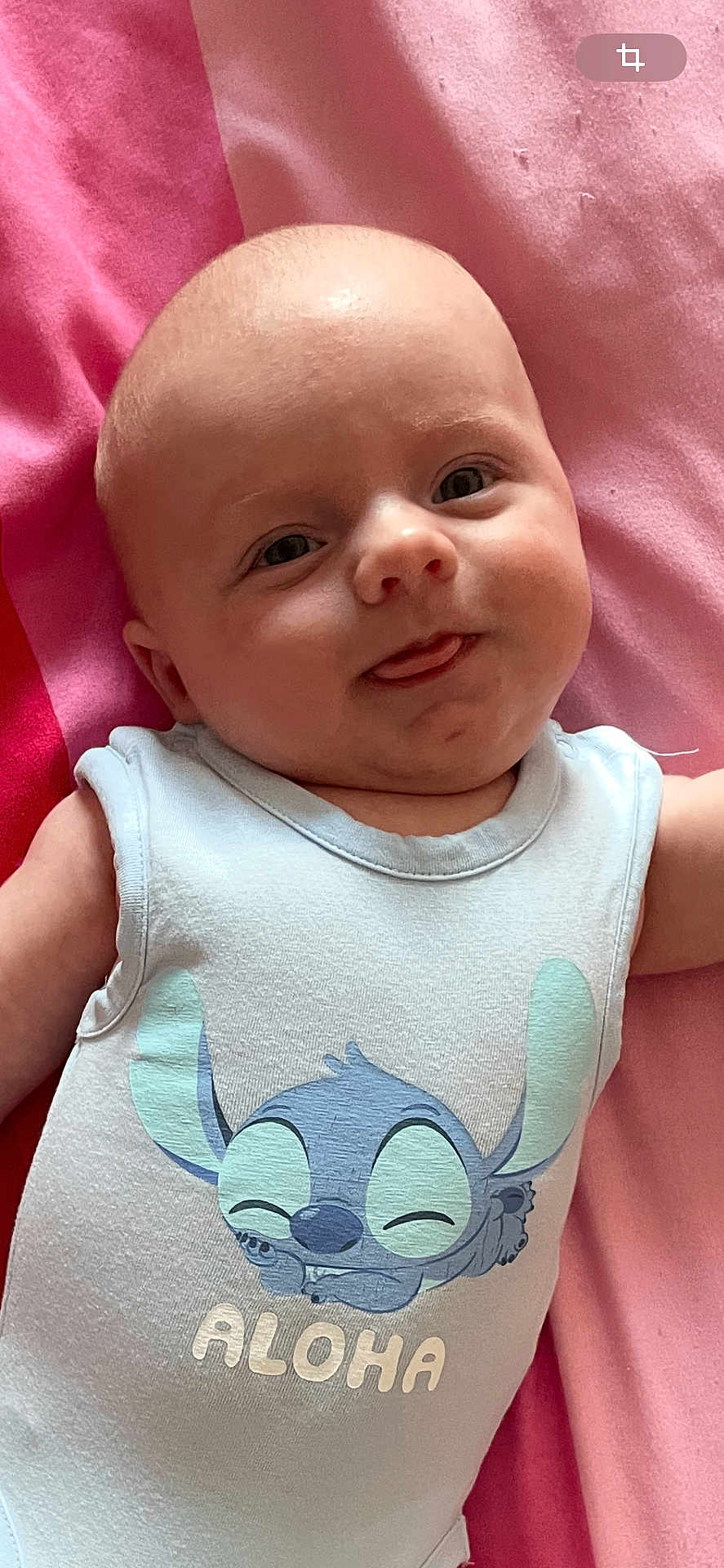 Amaury participe au concours pour gagner de l'argent avec cette photo : baby, infant, onesie, pink_blanket, cartoon_character, aloha, tongue_out, cute, smiling, child, clothing, fabric, face, skin, head, person, baby_garment, lying_down, playful, expression