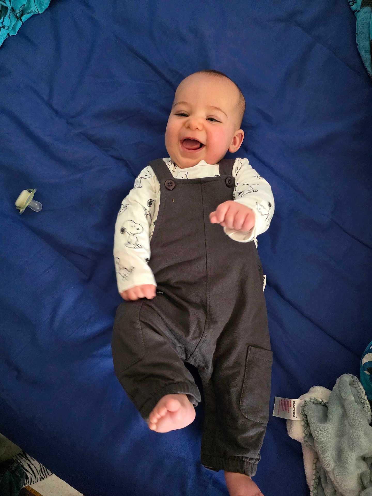 Mickaël participe au concours pour gagner de l'argent avec cette photo : baby, infant, smiling, laughing, face, overalls, onesie, blue_blanket, pacifier, lying_down, hand, foot, blanket, portrait, happy, indoor, clothing, chubby_cheeks, baby_sleeping_area, cute