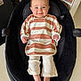 baby, child, smile, face, bib, striped_clothing, pants, feet, cushion, seat, indoor, brick_wall, happy, person, infant, head, skin, footwear_free, comfort, casual