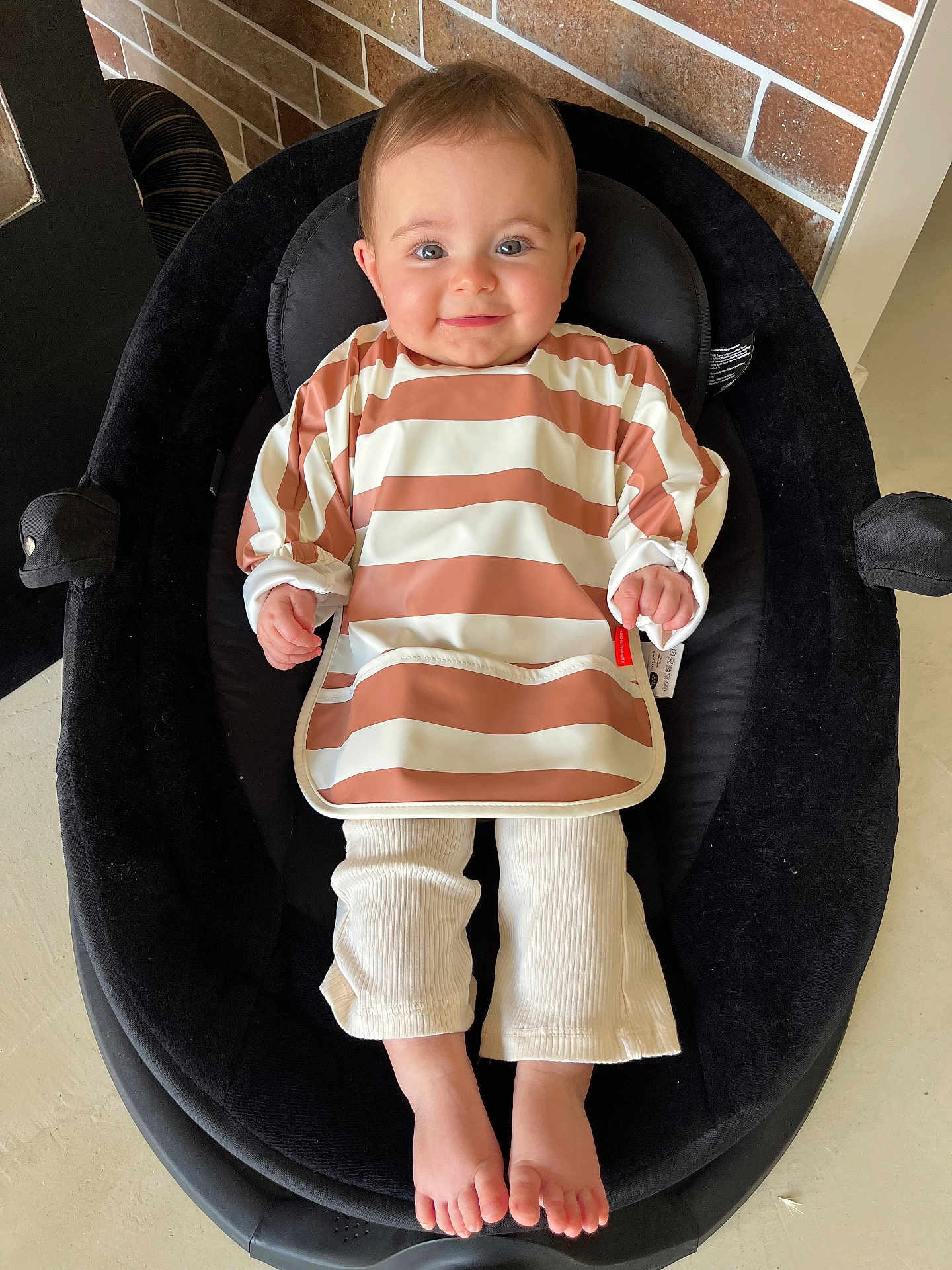 Alba a rejoint le concours — aidez-le/la à gagner de superbes lots ! baby, child, smile, face, bib, striped_clothing, pants, feet, cushion, seat, indoor, brick_wall, happy, person, infant, head, skin, footwear_free, comfort, casual