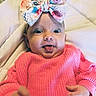 baby, infant, bow, headwear, pink_sweater, tongue_out, closeup, cute, child, playful, expression, soft_blanket, indoors, portrait, small_hands, wide_eyes, colorful, texture, happy, adorable
