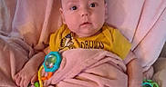 Benjamin joined the competition — help win amazing prizes! baby, blanket, toy, yellow_shirt, cushion, chair, infant, indoor, face, person, child, comfort, soft, cute, expression, holding, colorful, pink, seated, curious