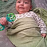 Benjamin is registered to the contest to win money with this photo: baby, infant, toy, rattle, blanket, pacifier, bed, smile, face, clothing, lying_down, green, pattern, child, cute, happy, indoors, soft, wrapped, playful
