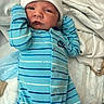 newborn, baby, infant, child, portrait, face, eyes_open, white_hat, blue_clothing, striped_outfit, onesie, mittens, blanket, bed, indoors, lying_down, cozy, hospital, close_up, photograph