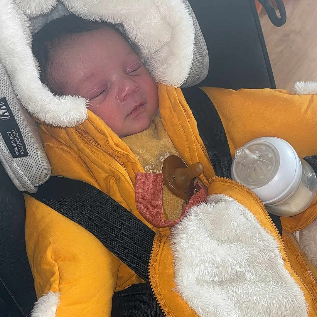 Maloyann a rejoint le concours — aidez-le/la à gagner de superbes lots ! baby, baby_bottle, car_seat, child, comfort, cozy, cute, face, fur_lined_hood, indoor, infant, jacket, newborn, pacifier, person, portrait, safety_harness, sleeping, warm_clothing, yellow_clothing