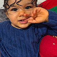 Maëna a rejoint le concours — aidez-le/la à gagner de superbes lots ! child, toddler, face, eyes, curly_hair, hair_bun, hand, finger, blue_sweater, smile, eyelashes, cheeks, lips, indoors, couch, red_cushion, portrait, close_up, skin, cute