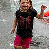 child, water, splash, fountain, running, wet, outdoor, play, fun, black_shirt, red_bow, pink_shorts, summer, water_play, happy, active, park, person, daytime, wet_hair