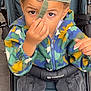 child, boy, stroller, cap, backwards_cap, camouflage_jacket, cargo_pants, curious, brown_eyes, hand, outdoor, footwear, seated, young, person, clothing, fabric, seat, straps, casual