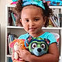 Myrtlelee is registered to the contest to win money with this photo: blue_headband, books, bookshelf, child, childhood, colorful, curly_hair, cute, furniture, happy, holding, indoor, person, playtime, plush_toy, portrait, room, smiling, toy, young_child