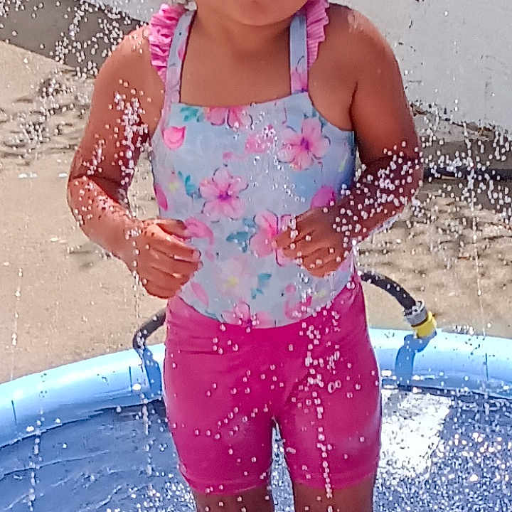Myrtlelee joined the competition — help win amazing prizes! barefoot, child, concrete, curly_hair, daytime, fun, garden_hose, girl, happy, outdoor, pink_shorts, play, pool, splash, summer, sunlight, swimsuit, water, water_droplets, white_wall