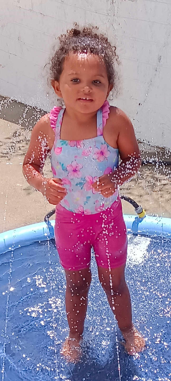 Myrtlelee joined the competition — help win amazing prizes! barefoot, child, concrete, curly_hair, daytime, fun, garden_hose, girl, happy, outdoor, pink_shorts, play, pool, splash, summer, sunlight, swimsuit, water, water_droplets, white_wall