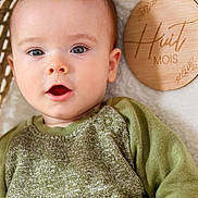 Livio a rejoint le concours — aidez-le/la à gagner de superbes lots ! baby, infant, child, face, eyes, mouth, sweater, green_sweater, wooden_plaque, milestone_marker, blanket, basket, portrait, skin, cheek, ear, cute, laying_down, indoor, close_up