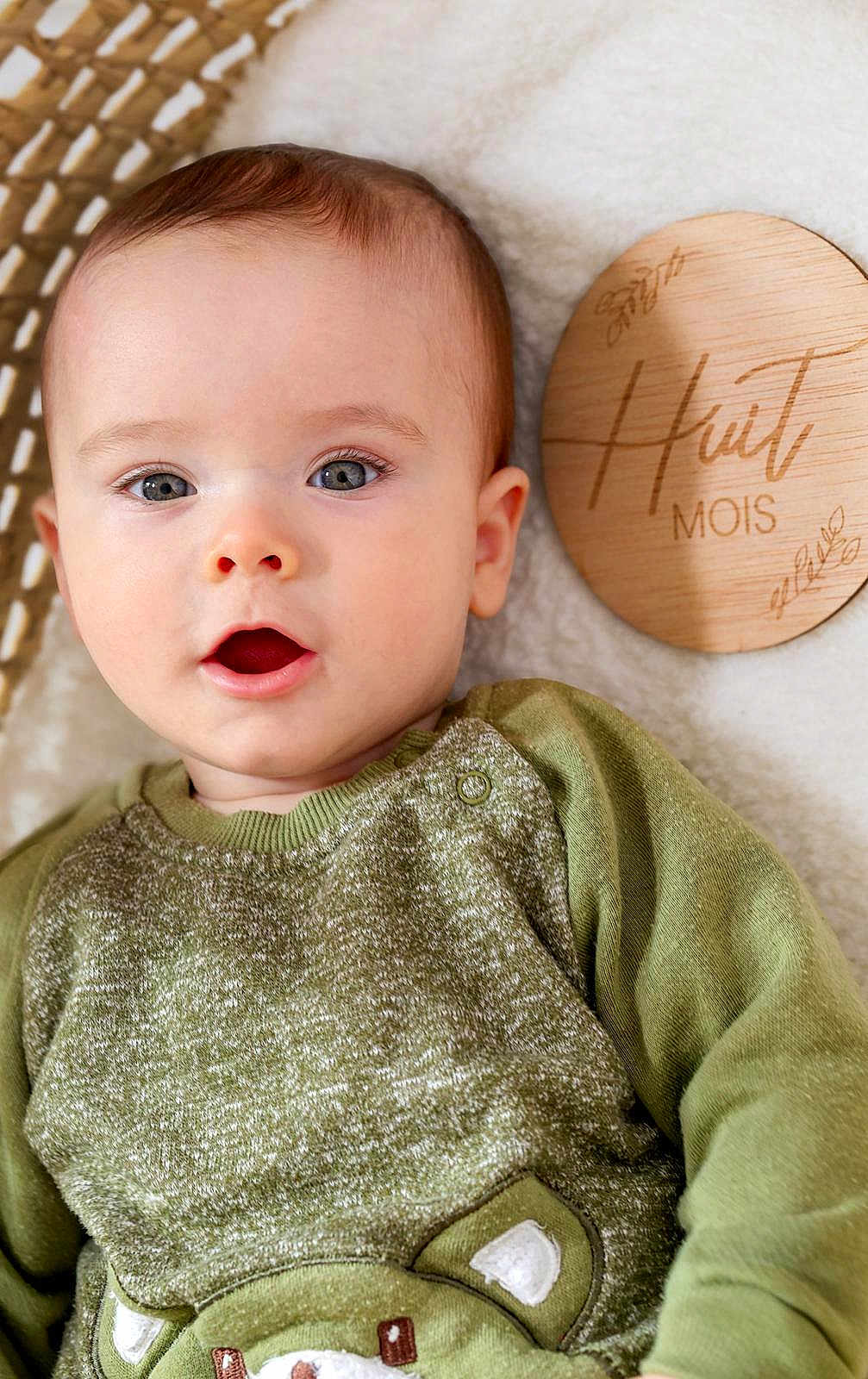 Livio a rejoint le concours — aidez-le/la à gagner de superbes lots ! baby, infant, child, face, eyes, mouth, sweater, green_sweater, wooden_plaque, milestone_marker, blanket, basket, portrait, skin, cheek, ear, cute, laying_down, indoor, close_up