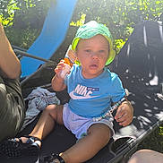 Lowen a rejoint le concours — aidez-le/la à gagner de superbes lots ! toddler, child, hat, blue_shirt, nike, sunscreen, bracelet, outdoor, garden, sunlight, chair, black_sandals, shorts, person, summer, relaxing, beads, greenery, sunny, daytime