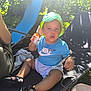 toddler, child, hat, blue_shirt, nike, sunscreen, bracelet, outdoor, garden, sunlight, chair, black_sandals, shorts, person, summer, relaxing, beads, greenery, sunny, daytime