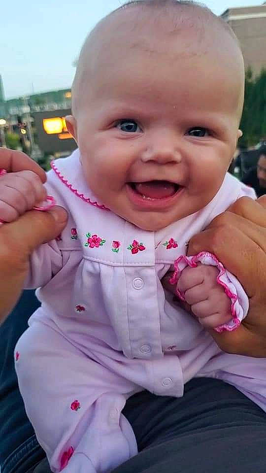 Brianna is registered to the contest to win money with this photo: baby, baby_toddler_clothing, blurred, cheek, face, facial_expression, finger, fun, gesture, grass, hand, happy, lip, mouth, nose, person, pink, skin, sleeve, smile